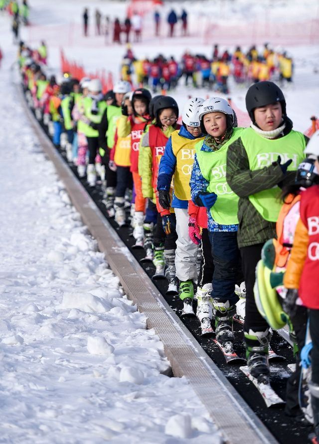 在吉林北大壶滑雪场，吉林市第二实验小学学生们在滑雪教练的带领下乘坐“魔毯”前往雪场学习区域。